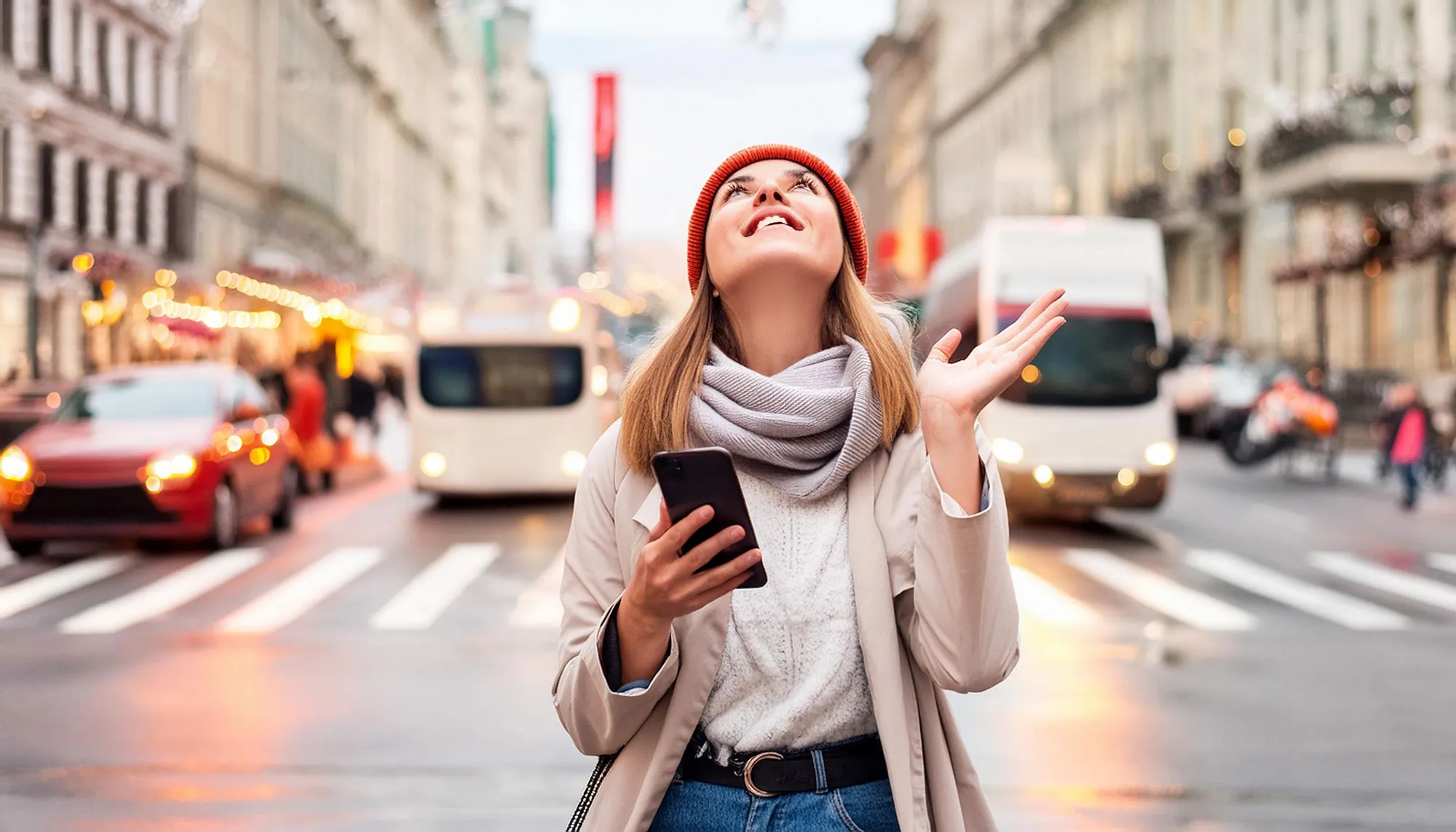 Eine Person ist dankbar über eine gute Nachricht auf dem Smartphone, steht im Verkehr und blickt nach oben.