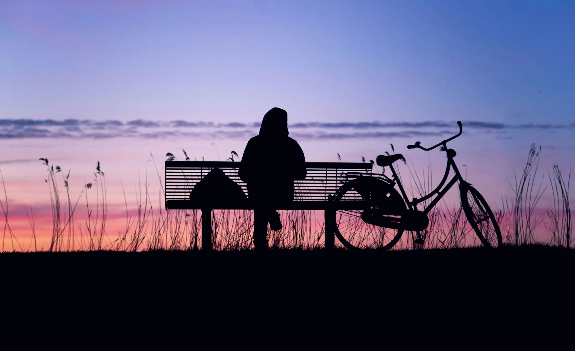 Silhouette einer Person, die beim Sonnenuntergang auf einer Bank sitzt
