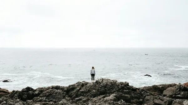 Frau steht auf Felsen vor dem Meer
