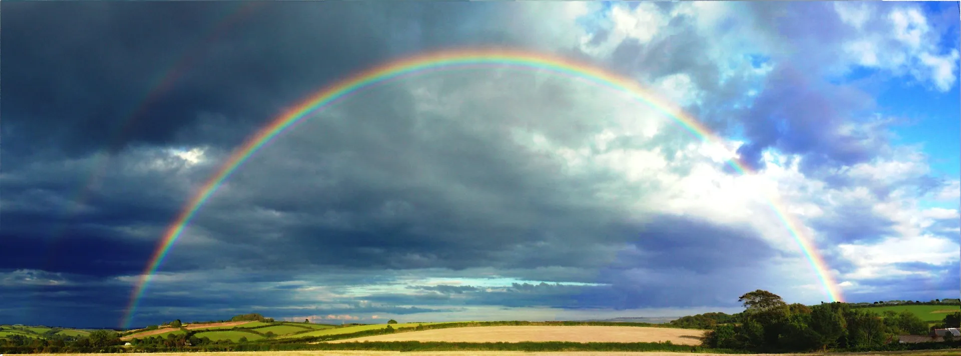 Regenbogen über Feld bewölkter Himmel