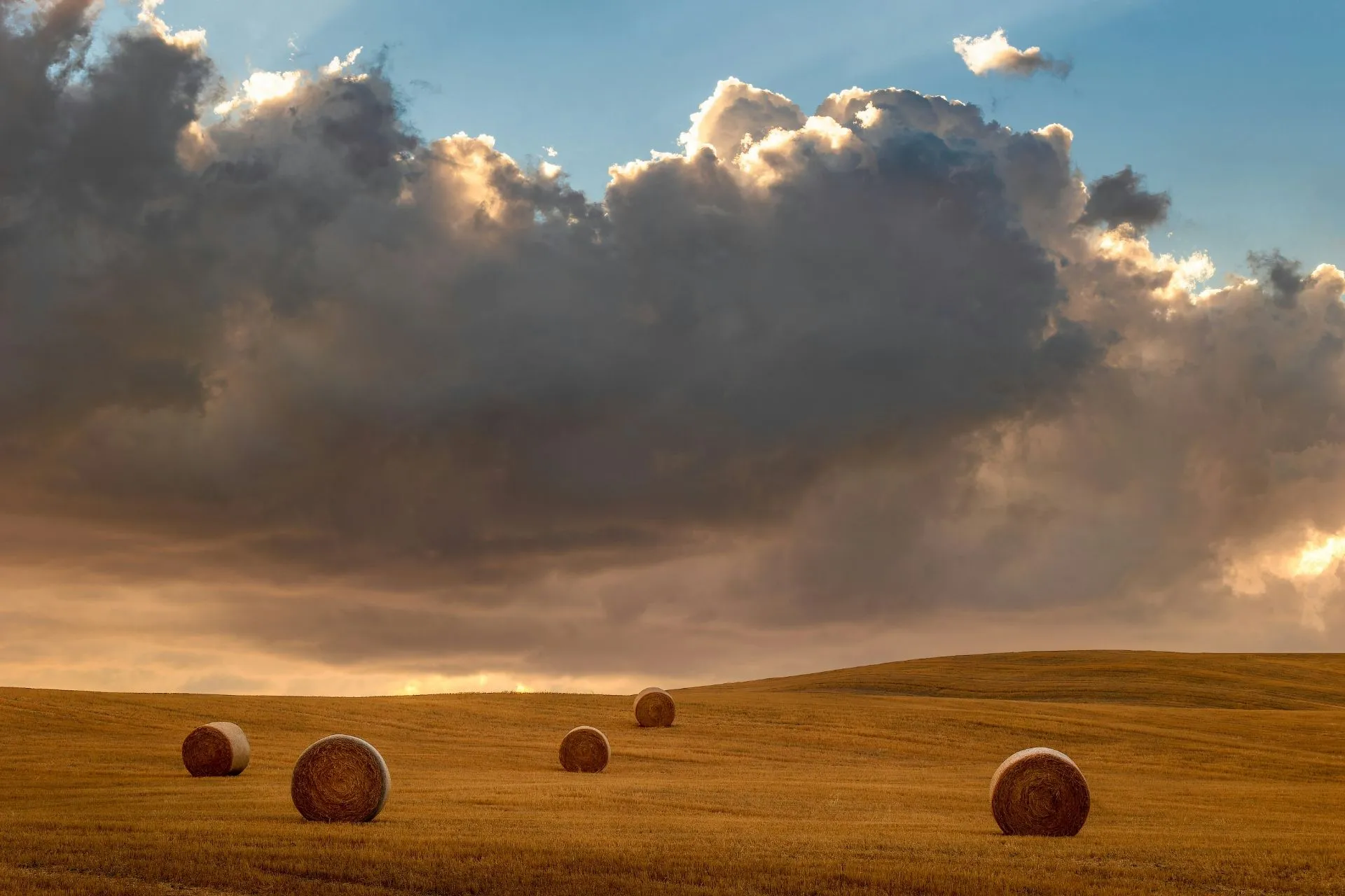 Abgeerntetes Feld mit Heuballen und stark bewölktem Himmel