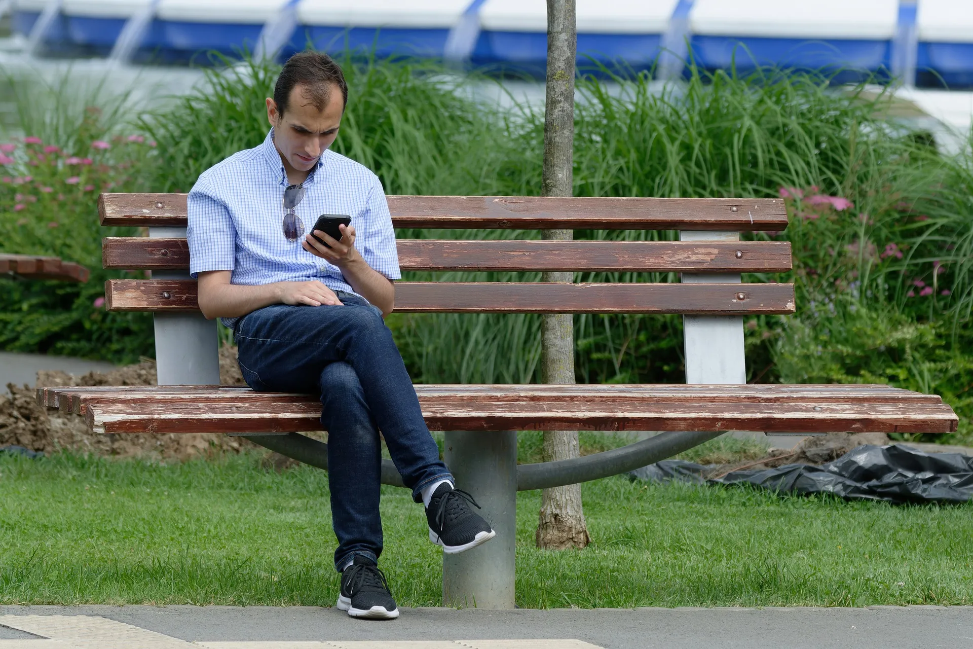 Mann sitzt auf Parkbank mit Handy in der Hand
