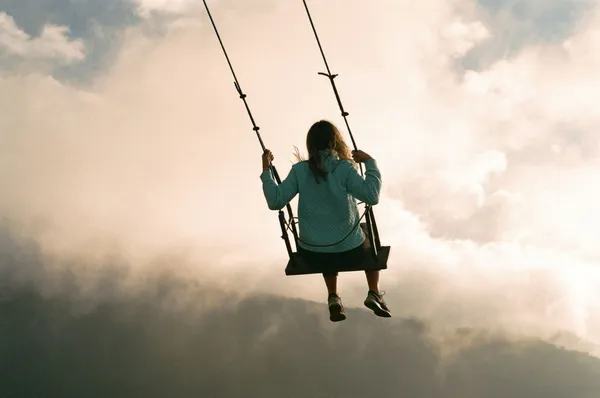 Mädchen auf einer Schaukel mit Blick in den Himmel