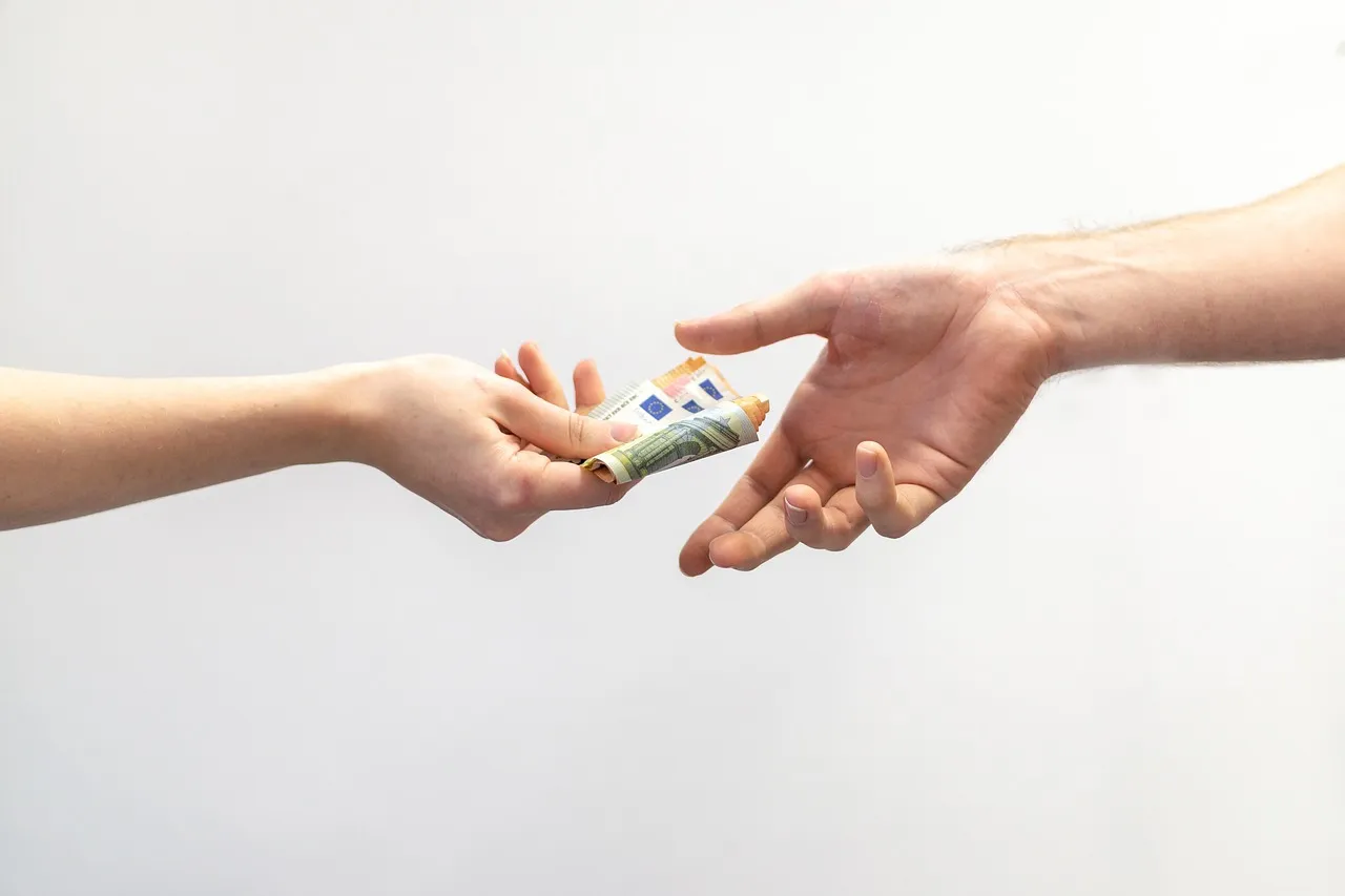 Eine Hand übergibt einer anderen Hand eine Rolle Gelscheine