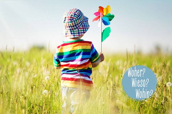 Kind mit Windrad in einer Wiese und Frage: Woher? Wieso? Wohin?