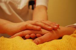 Ein:e Klinikmitarbeiter:in hält die Hand einer kranken Person