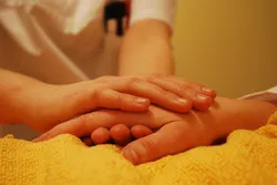 Ein:e Klinikmitarbeiter:in hält die Hand einer kranken Person