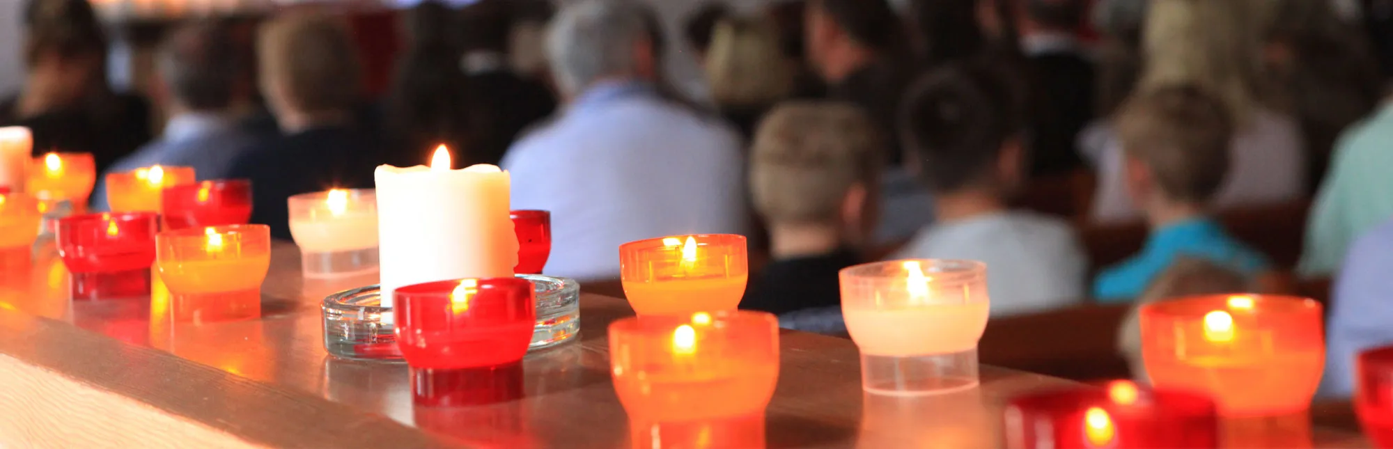 Brennende Teelichter im Vordergrund und Gottesdienstbesuchende im Hintergrund