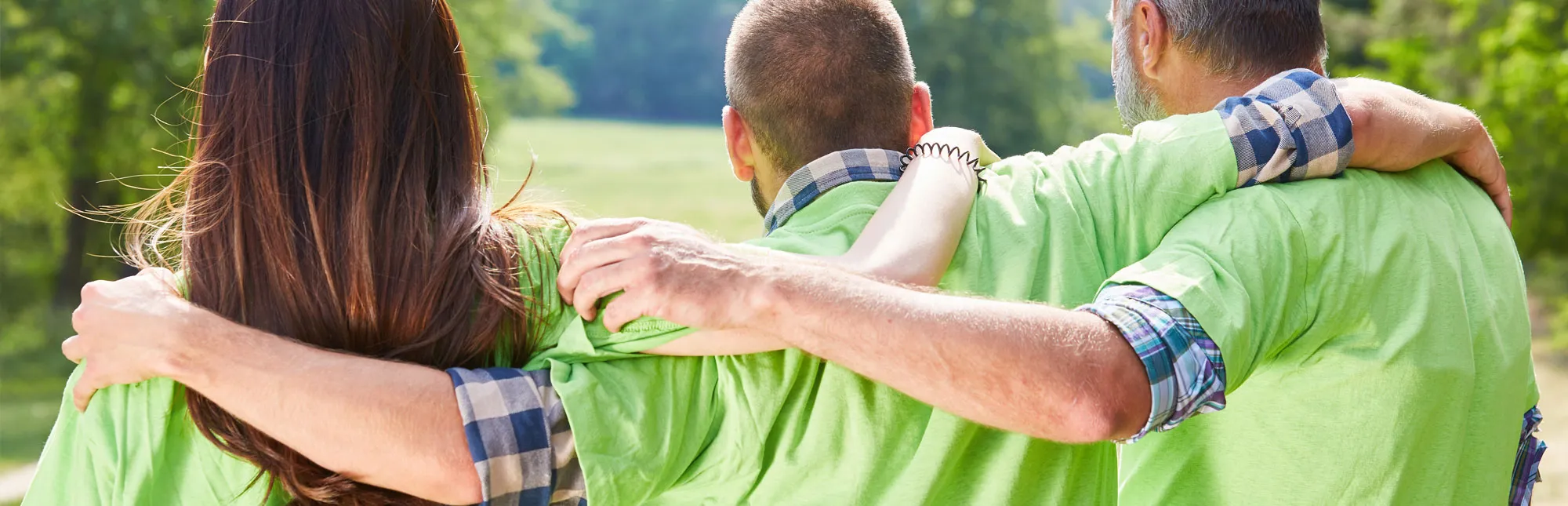 Drei Menschen von Hinten, die sich die Hände auf die Schultern gelegt haben