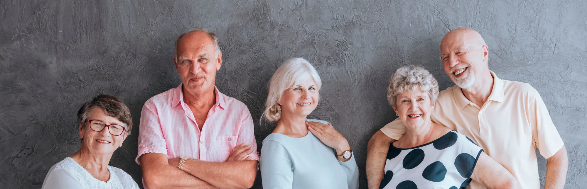 Fünf Senioren und Seniorinnen stehen nebeneiander vor einer Wand.