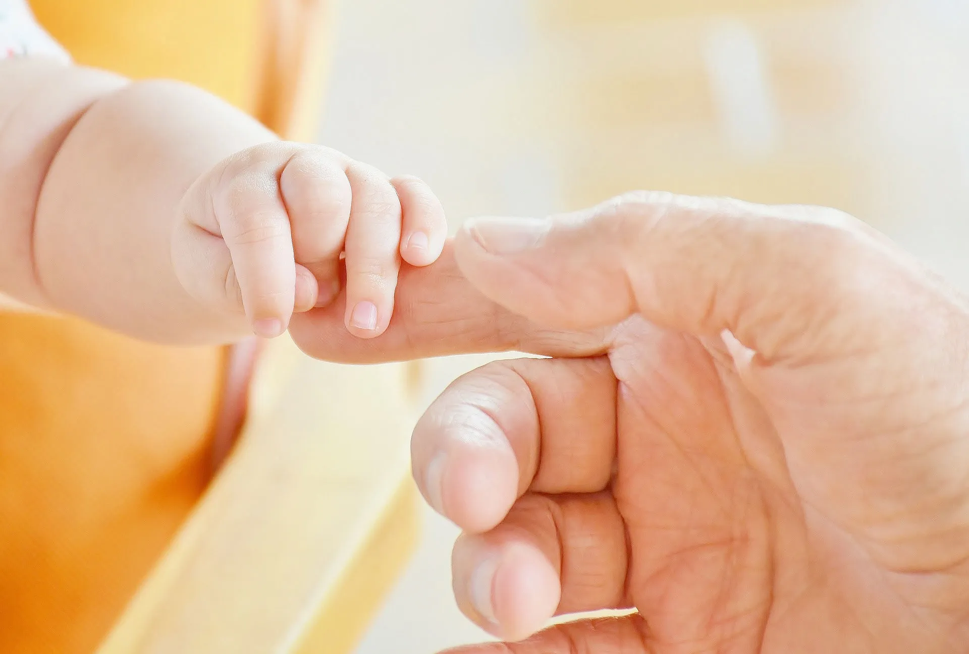 Eine Babyhand hält den Finger eines erwachsenen Menschen.