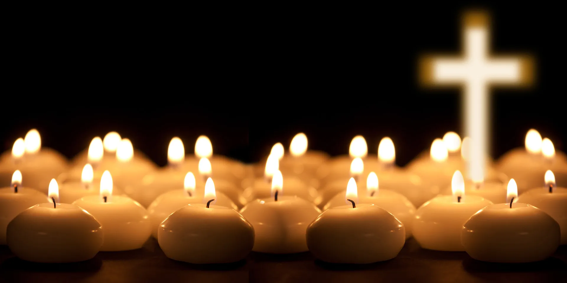 Viele brennende Kerzen und ein Kreuz unscharf im Hintergrund