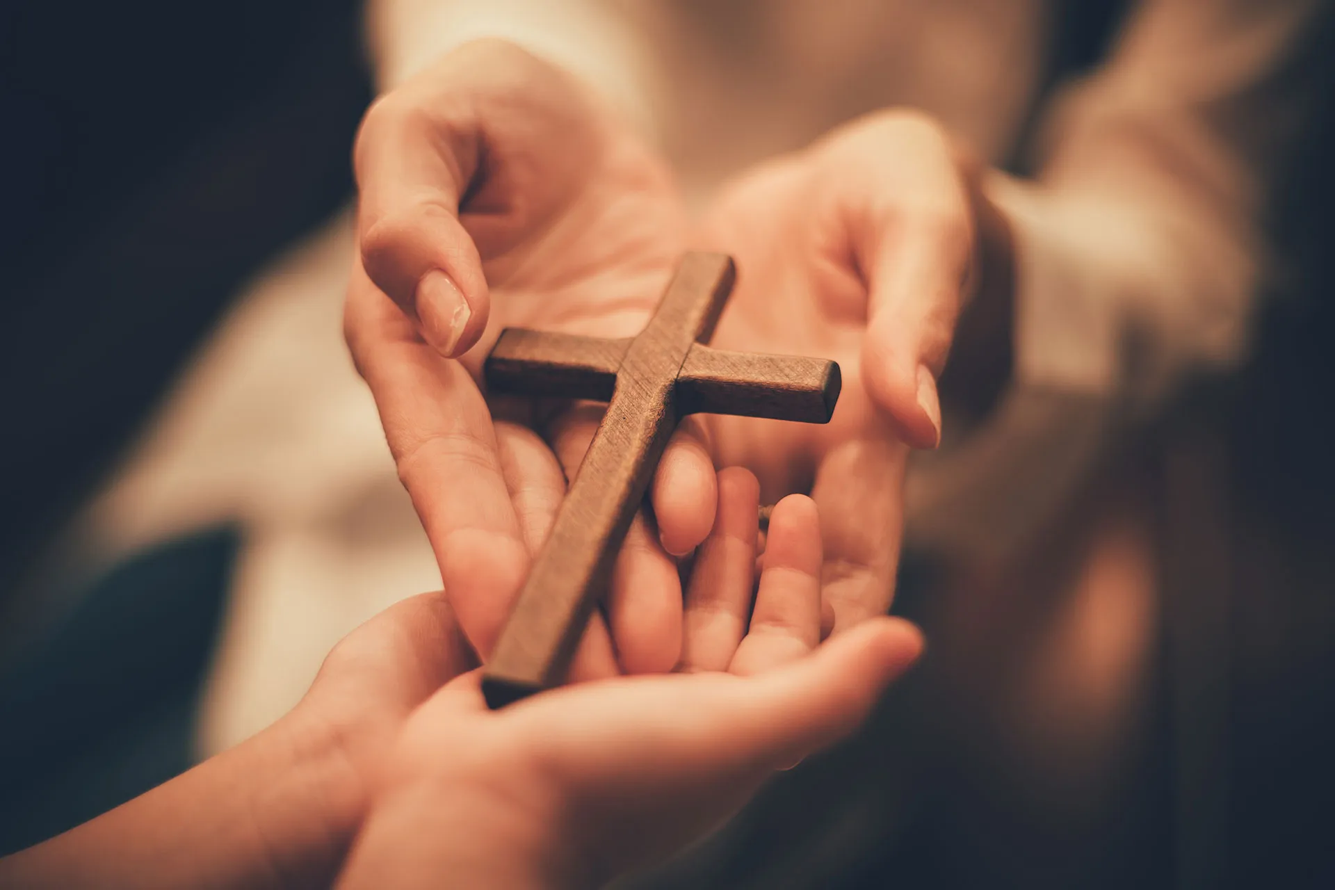 Zwei Hände halten ein Holzkreuz