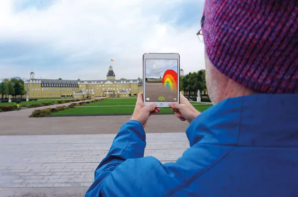 Eine Person setzt mit ihrem iPad einen virtuellen Regenbogen vor das Karlsruher Schloss.