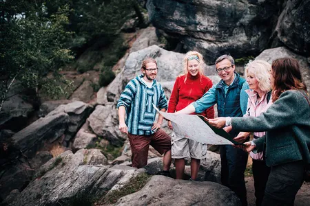 Eine Gruppe von Menschen steht im Wald und blickt gemeinsam auf eine Landkarte
