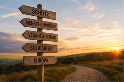 Feldweg bei Sonnenuntergang, im Vordergrund ein Wegweiser. Ausgeschildert sind "Schutz", "Menschenwürde", "Verantwortung", "Solidarität" und "Europa"