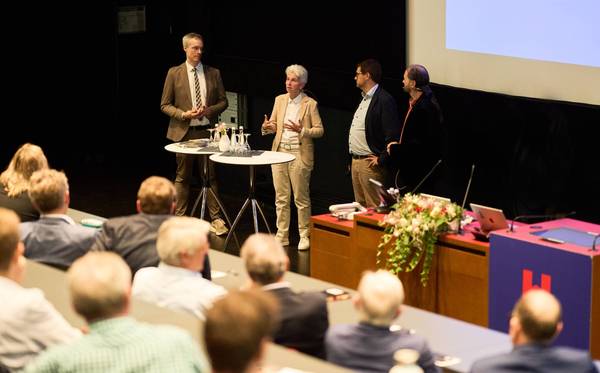 Publikum im Vordergrund schaut der Diskussion zwischen Gerhard Schreiber, Amrie-Agnes Strack-Zimmermann, Tobias Kreilos und Gernot Meier zu
