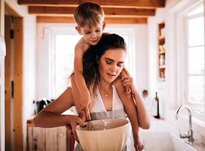 kleiner Junge sitzt auf Muttersschulter und rührt in der Schüssel