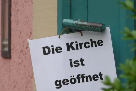 Quelle: EOK/Stabsstelle DiakonInnen/AEller Kirchentür geöffnet, an der Türklinke hängt ein Schild mit Aufschrift "Die Kirche ist geöffnet"