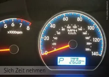 auf dunklem Hintergrund ein blau rötlich schimmender Autotach mit gelben Pfeil der auf die null zietgt am unteren Rand ein weißes Feld mit  links ein großen PP und rechts untereinander TRIP A 260,8 danaeben ein Drehzahlmeesser nur teilweise zu sehen. Datunter der Worte: "Sich Zeit nehmen"