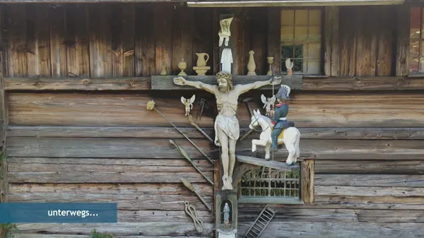 Quelle: Evangelischer Rundfunkdienst Baden ERB Holzgeschnitzte und bunt bemalte Kreusdarstellung an der Fassade des Hippenseppenhof im Schwarzwälder Freilichtmuseum Vogtsbauernhof in Gutach.