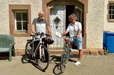 Die beiden Seelsorger*innen stehen mit ihren Fahrrädern abfahrtbereit vo einem Haus