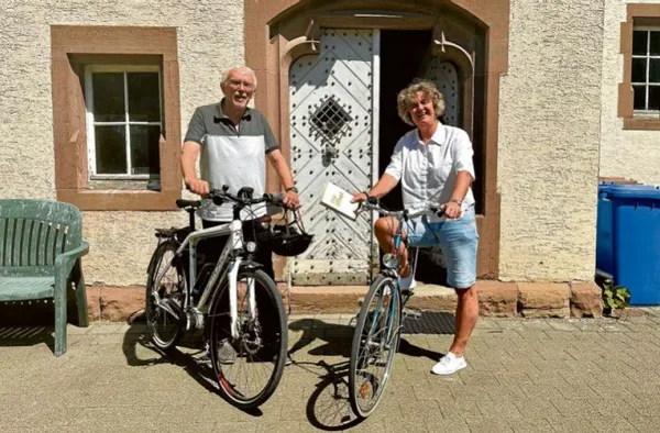 Die beiden Seelsorger*innen stehen mit ihren Fahrrädern abfahrtbereit vo einem Haus