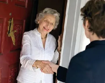 Eine ältere Frau steht im Trrahmen einer offenen Tür und begüßt eine andere Frau mit Handschlag, die vor der Tür steht.