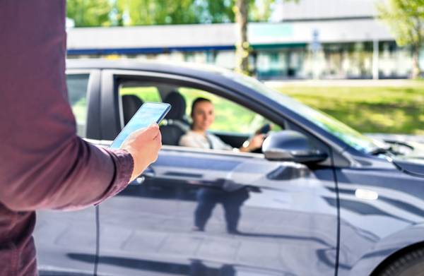 Person läuft mit Smartphone auf stehendes Auto hinzu