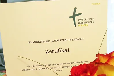 Quelle: EOK/Stabsstelle DiakonInnen/AEller Zertifikat Abschluss Traineeprogramm, davor eine Rose