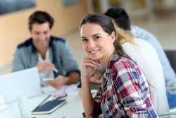 Quelle: Fotolia_57985017 Gruppe Student:innen am Tisch, im Vordergrund junge Frau mit Blick zur/m Betrachter:in