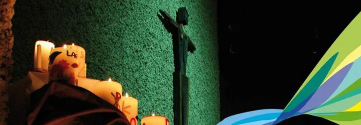 Bild: Grüne Wand mit Kreuz davor und brennde selbstgestaltete Kerzen