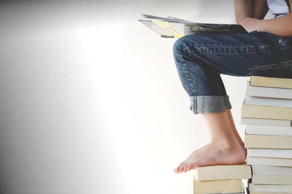 Person sitzt auf Bücherstapel und liest